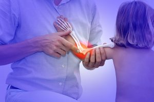 doctor is examining a young child's elbow, with the child's skeletal structure highlighted, showing the location of an injury